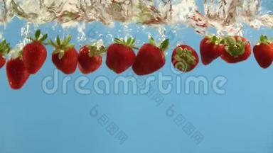 成熟的草莓在蓝色背景下落入水中。 夏季浆果在液体中